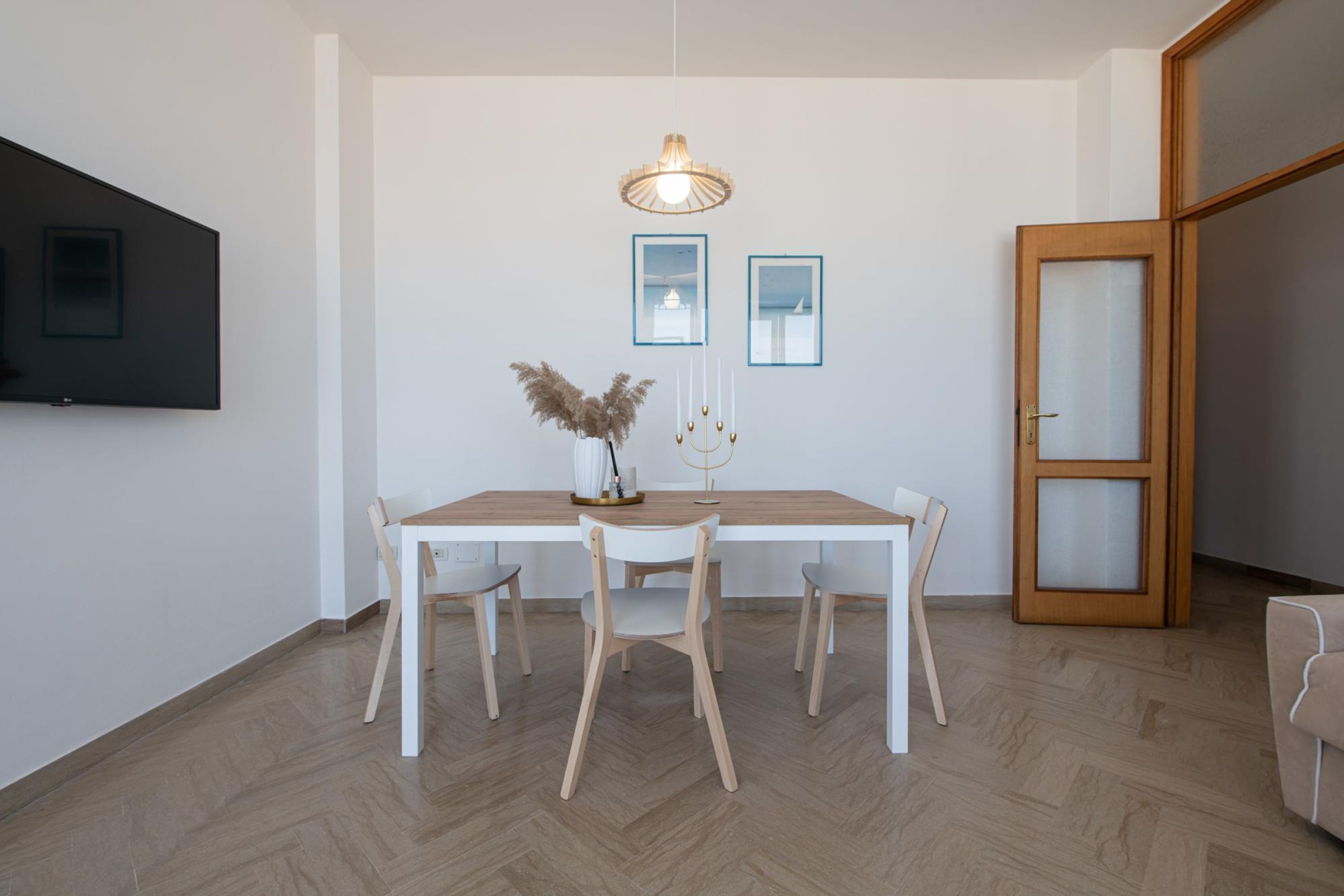 Et spiseområde med et træbord og stole, en hængende lampe og billeder i rammer på væggen.