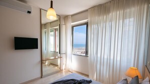 Une chambre d’hôtel avec un lit, une télévision, une fenêtre donnant sur la plage et une lampe.