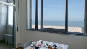 Une table de petit-déjeuner offrant une vue sur la plage et l’océan grâce à de grandes fenêtres.