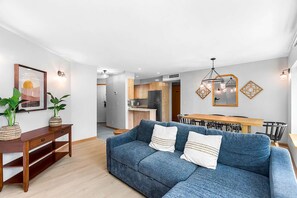 A modern living room with a sofa, a wooden console table, and a dining area with a table and chairs.