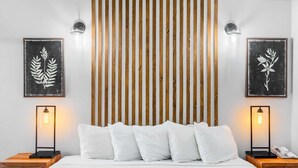 Ein modernes Schlafzimmer mit einer Wand aus Holzlamellen, einem großen Bett mit weißer Bettwäsche, zwei Nachttischen mit Lampen und gerahmten Pflanzenbildern an den Wänden.