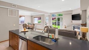 A modern kitchen with a central island, a dining area with chairs, and a sofa. - Icicle Village 2-Bedroom w/ Pool (Leavenworth)