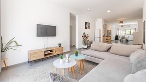 Un salon moderne avec un canapé, un téléviseur et un coin repas à l’arrière-plan.