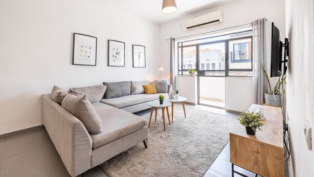Un salon moderne avec un canapé gris, une petite table ronde et un téléviseur posé sur un meuble en bois.