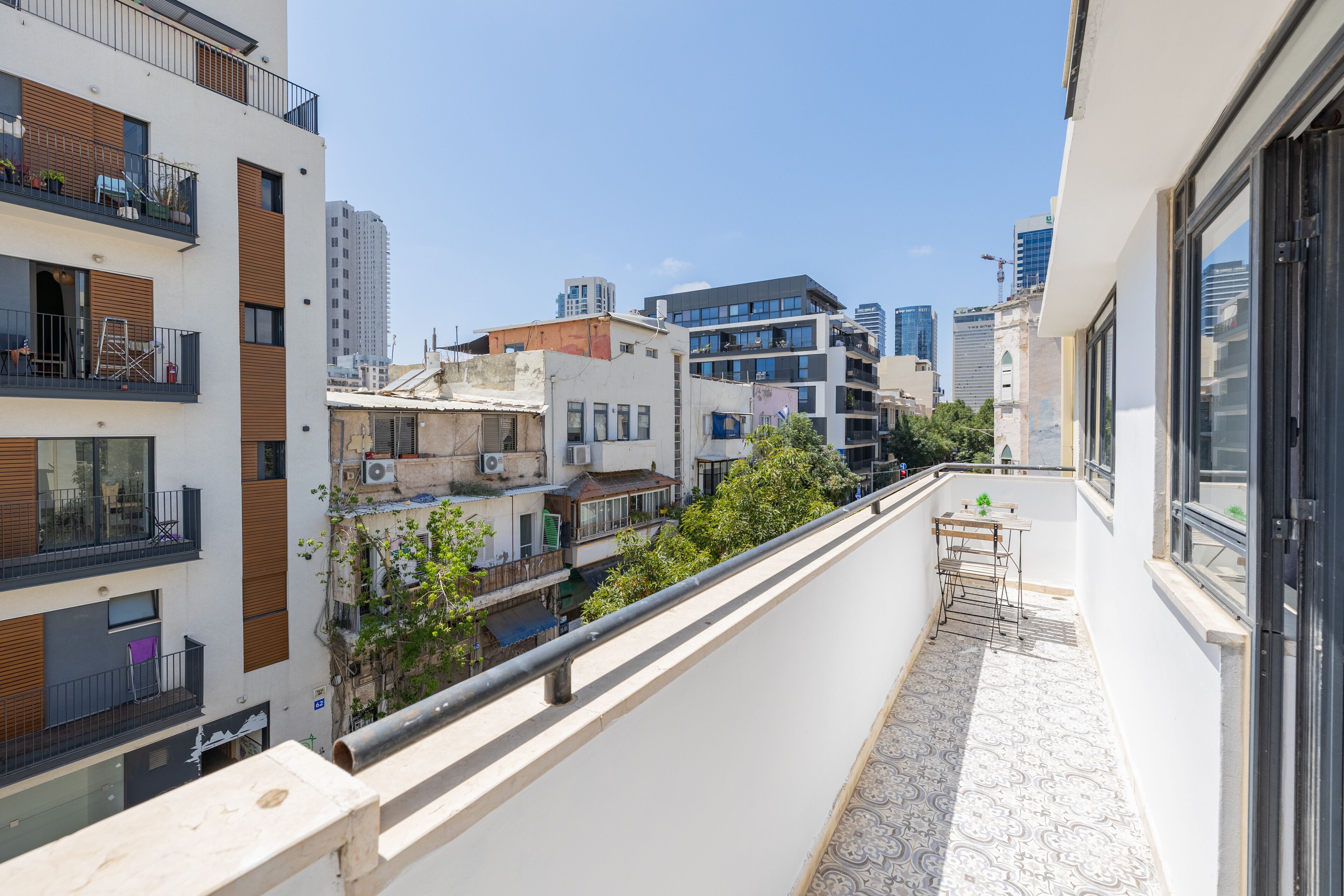 A balcony with a view of a cityscape, including modern and older buildings, and a small table with chairs.