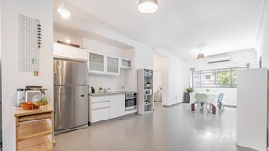 Une cuisine moderne avec des meubles blancs, des appareils en acier inoxydable et une table en bois accompagnée de chaises.