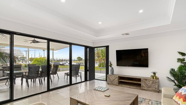 A modern living room with a large TV, a dining area with chairs, and a view of the outdoors. - Water Lovers Haven in Mandurah (Halls Head)