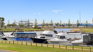 A marina with several boats docked, a grassy area, and buildings in the background. - Water Lovers Haven in Mandurah (Halls Head)
