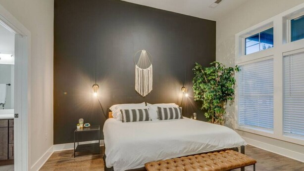 Ein Schlafzimmer mit einem großen Bett, Nachttischlampen, einer Bank, einer Wandleuchte und einer Zimmerpflanze.