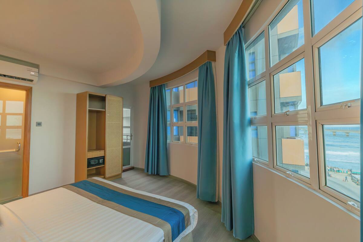 A hotel room with a bed, a wardrobe, a mirror, and a window with curtains.