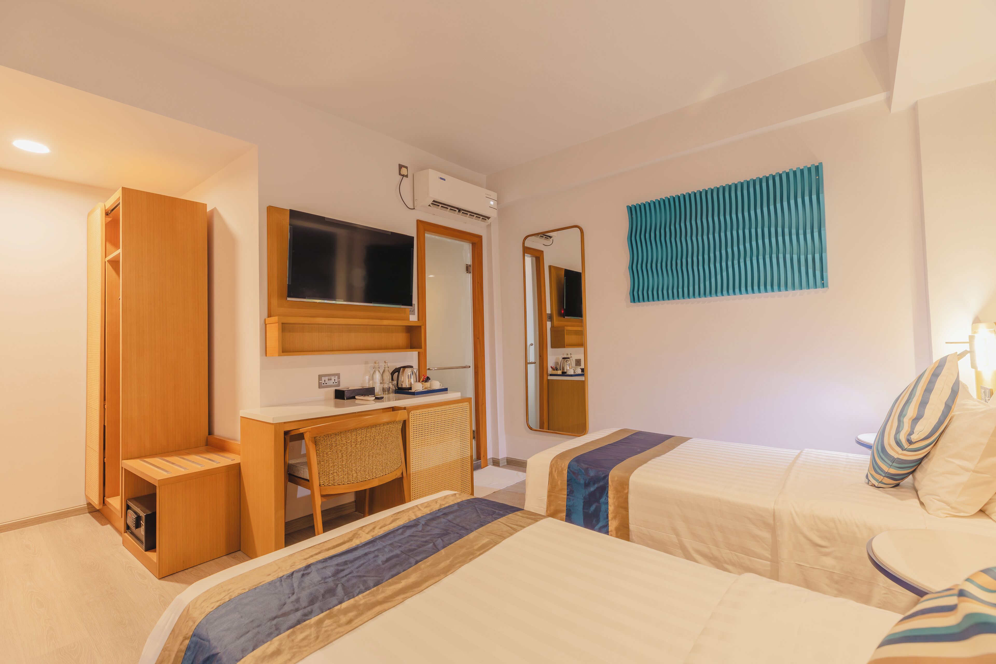 Habitación de hotel con dos camas, un escritorio, una silla, un espejo y un equipo de aire acondicionado.