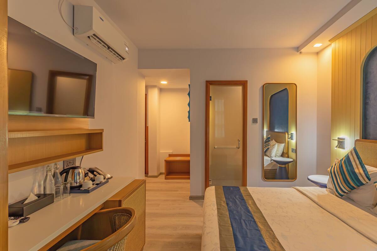 A hotel room with a bed, bedside table, TV, and a mirror.