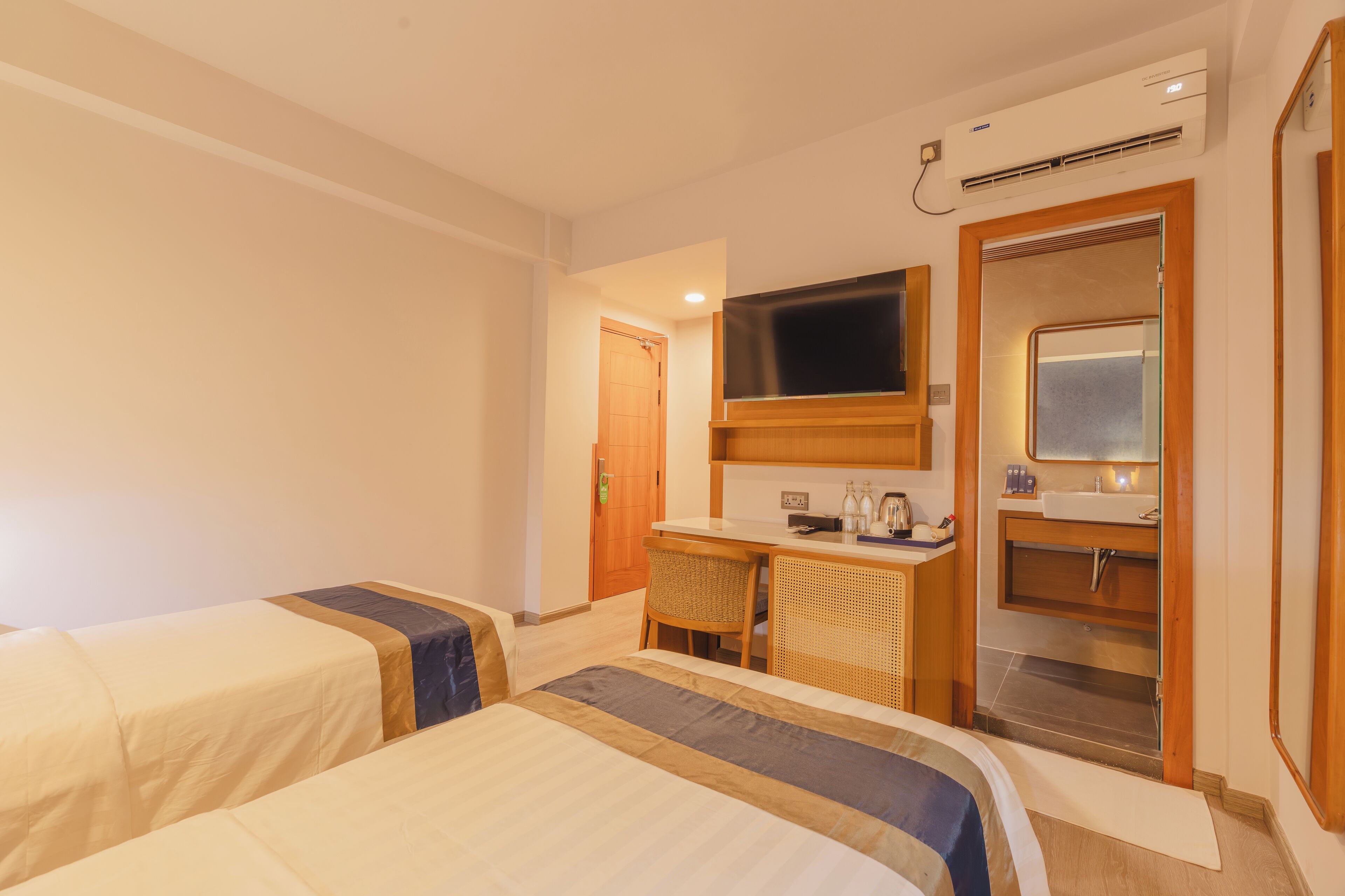 Ein Hotelzimmer mit zwei Betten, einem Schreibtisch, einem Fernseher und einem Badezimmer mit Spiegel und Waschbecken.