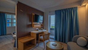 A modern hotel room with a wooden desk, a television, a sofa, and a balcony with blue curtains.