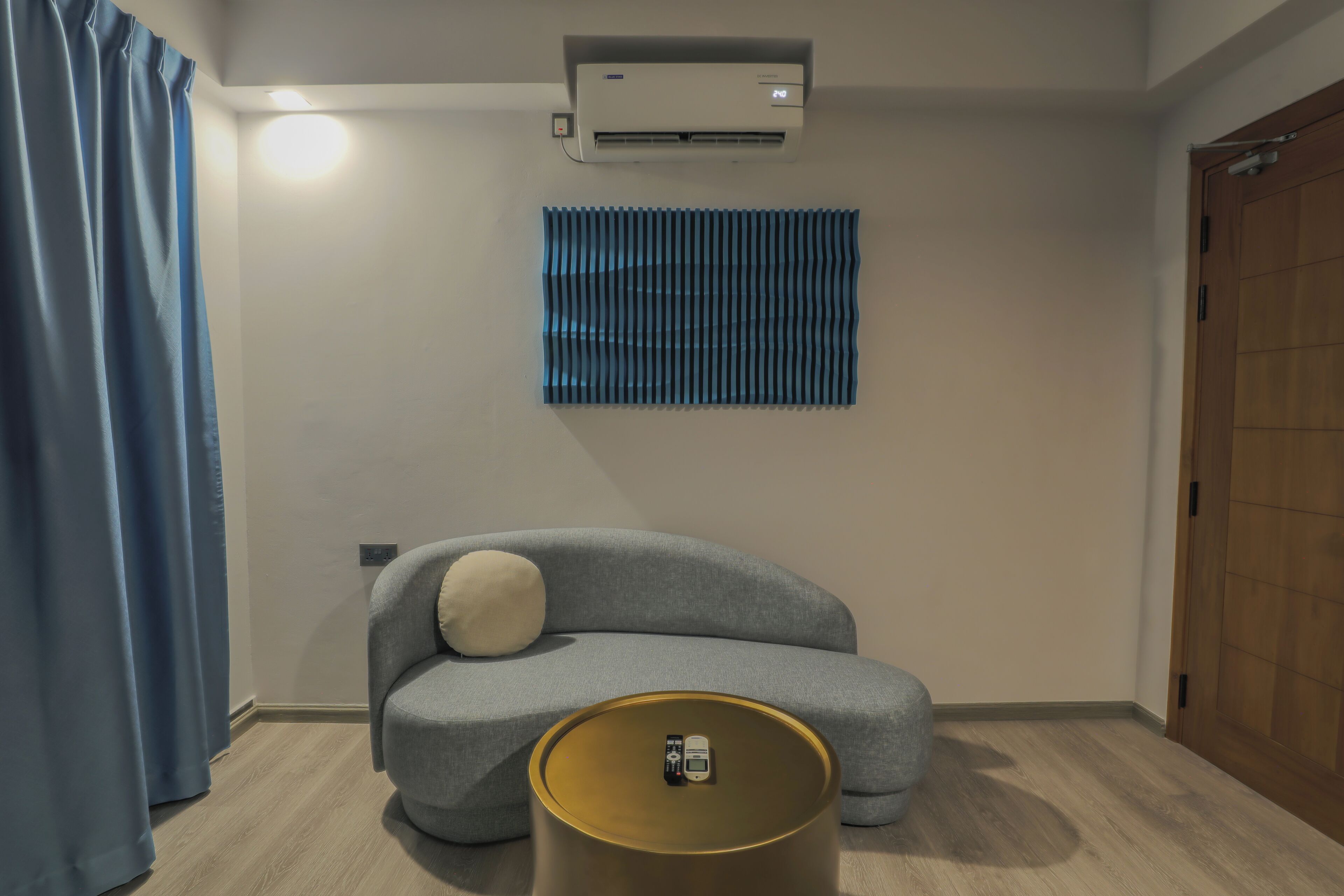 A modern room with a grey sofa, a small round table, a wall-mounted air conditioner, and a wooden door.