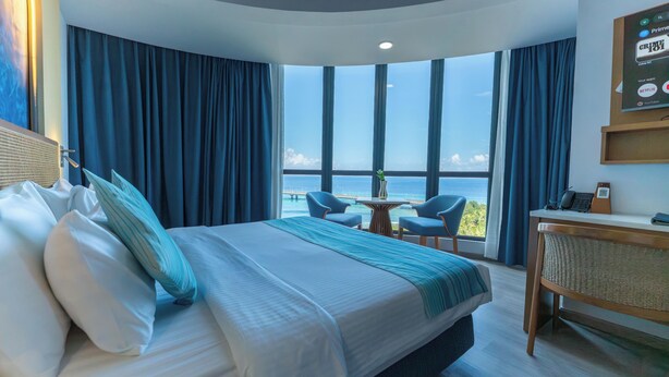 A hotel room with a large bed, a desk, a chair, and a view of the ocean.