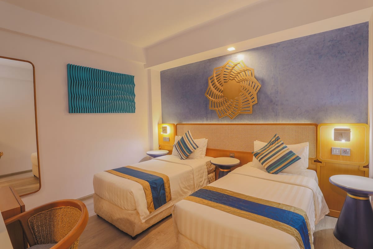 A hotel room with two beds, a small round table, a chair, and a decorative wall piece.