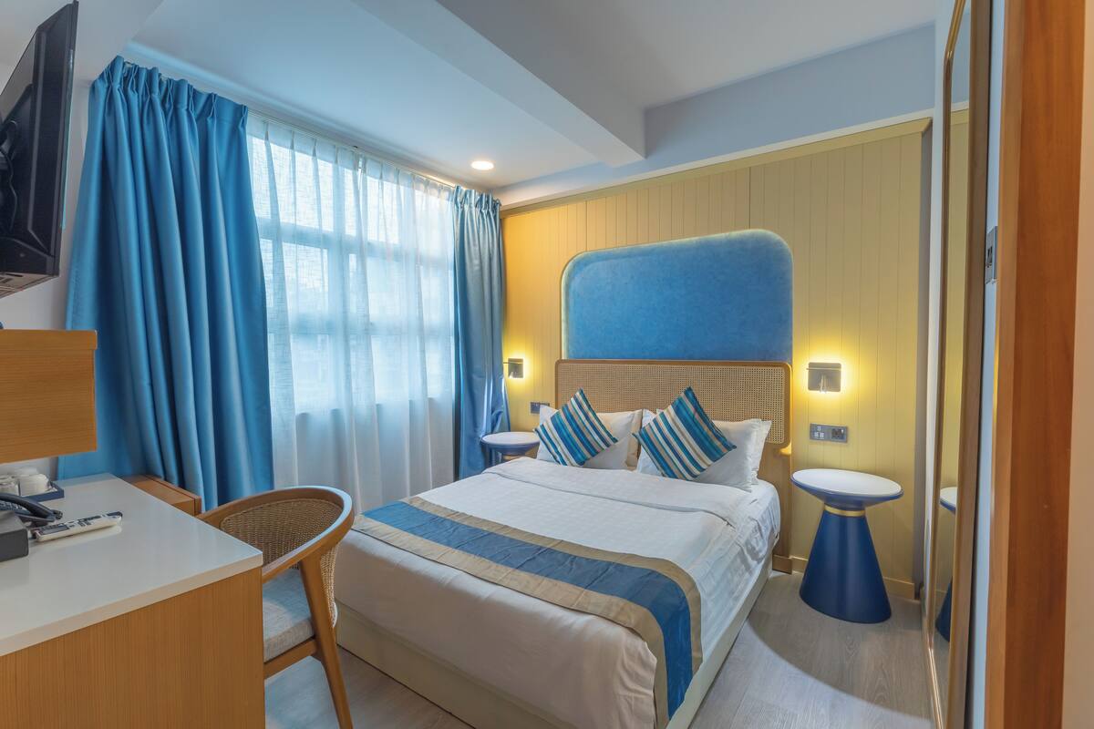 A hotel room with a bed, bedside tables, a desk, a chair, and a television.