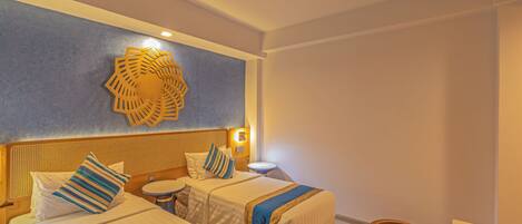 A hotel room with two beds, a round table, a wicker chair, and a decorative wall piece.