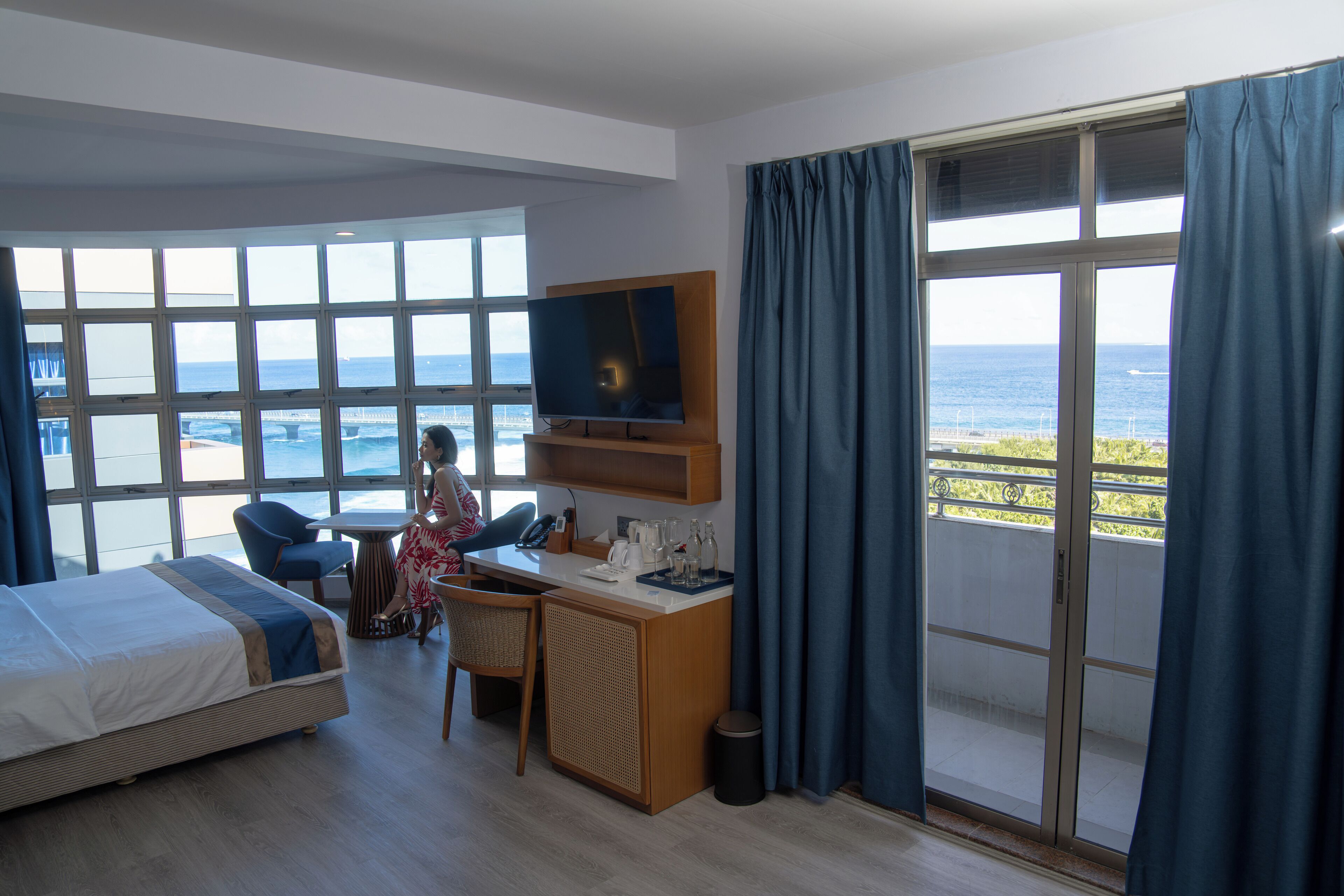 Una habitación de hotel con cama, escritorio, silla, televisión y vista al mar.