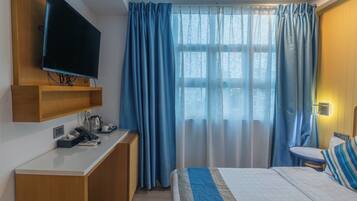 A hotel room with a bed, a desk with a telephone, a television mounted on the wall, and a window with curtains.