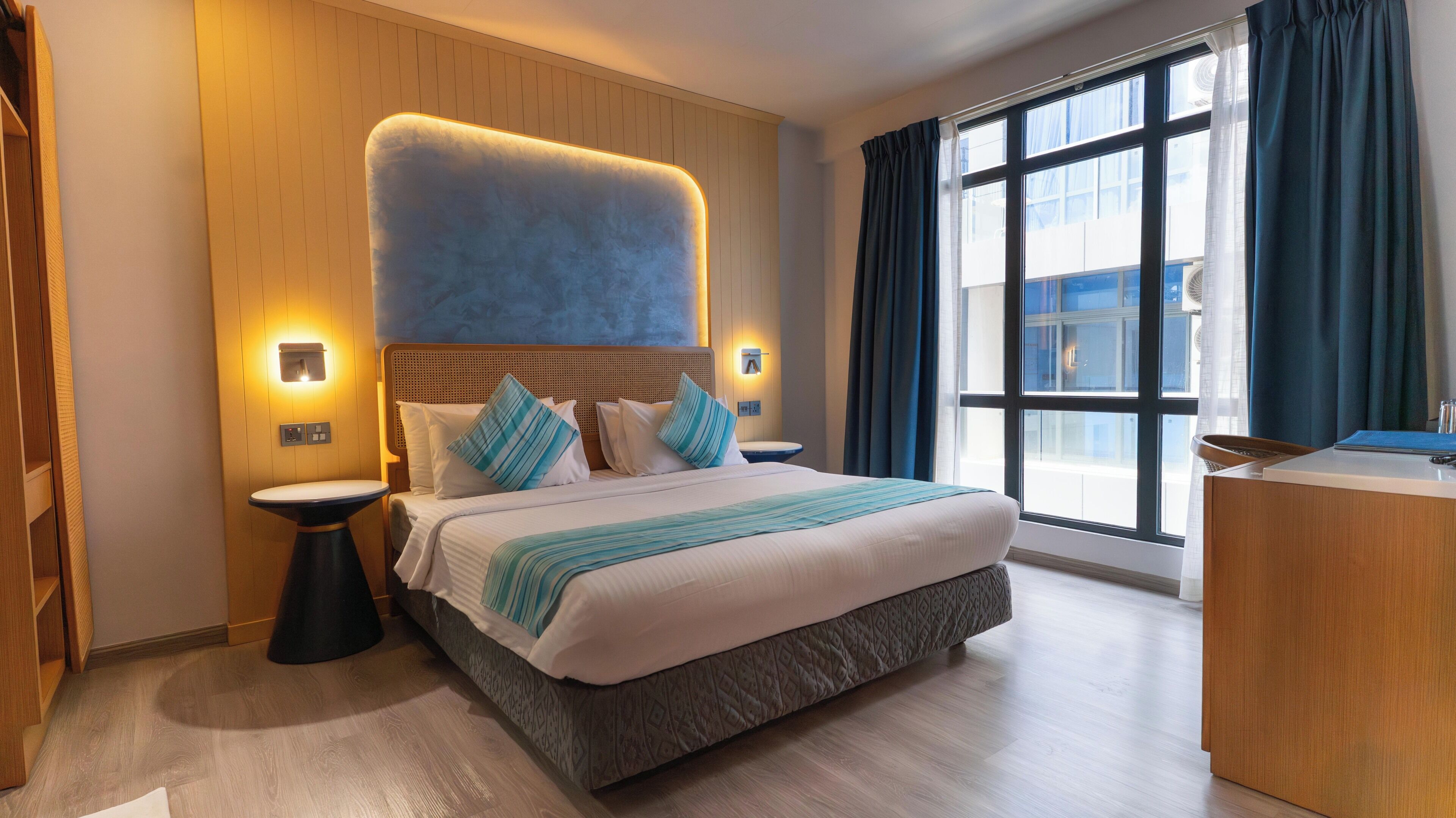 A hotel room with a large bed, bedside tables, a desk, and a window with curtains.