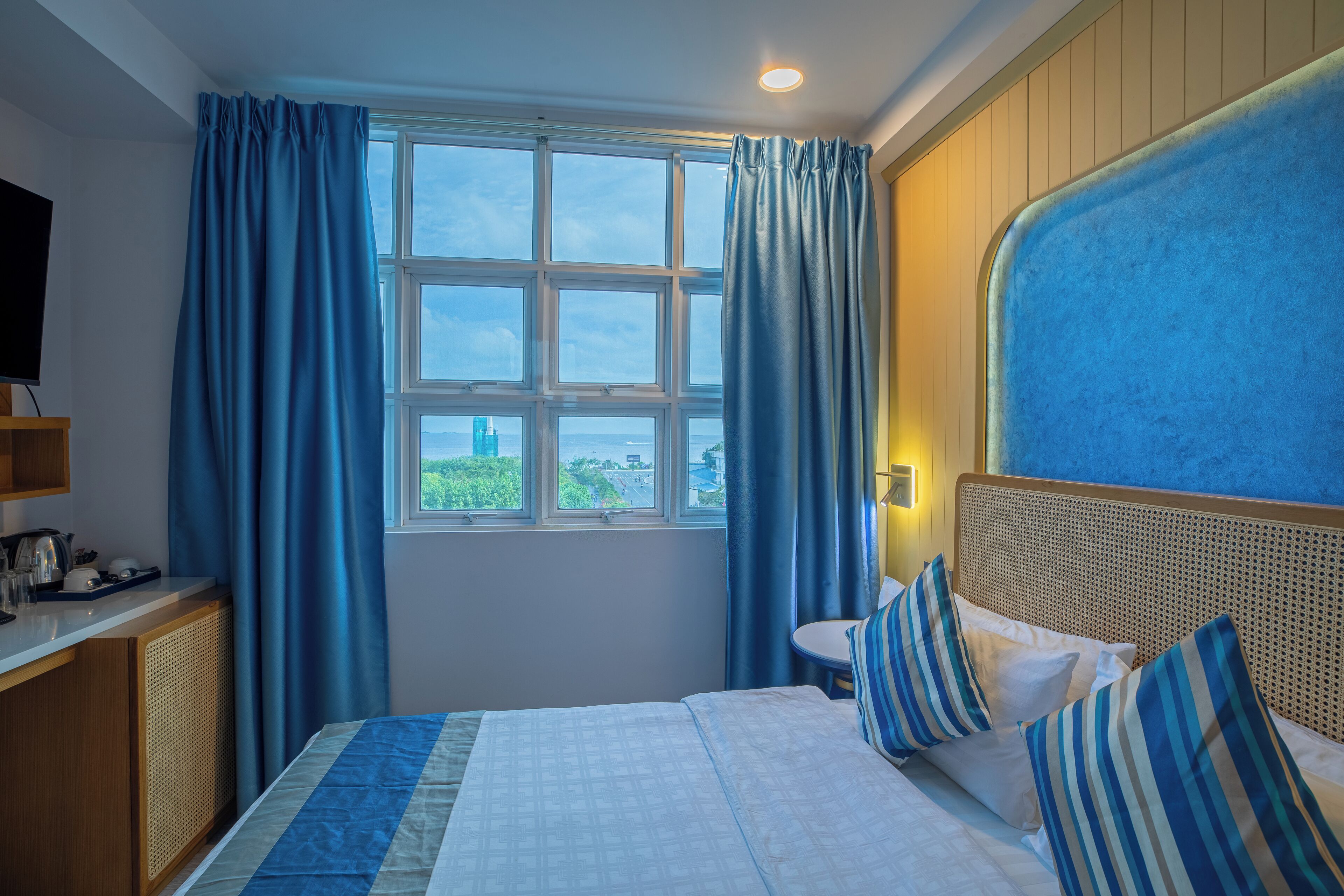 A hotel room with a large bed, a television on a wooden cabinet, a window with curtains, and a view of the cityscape.