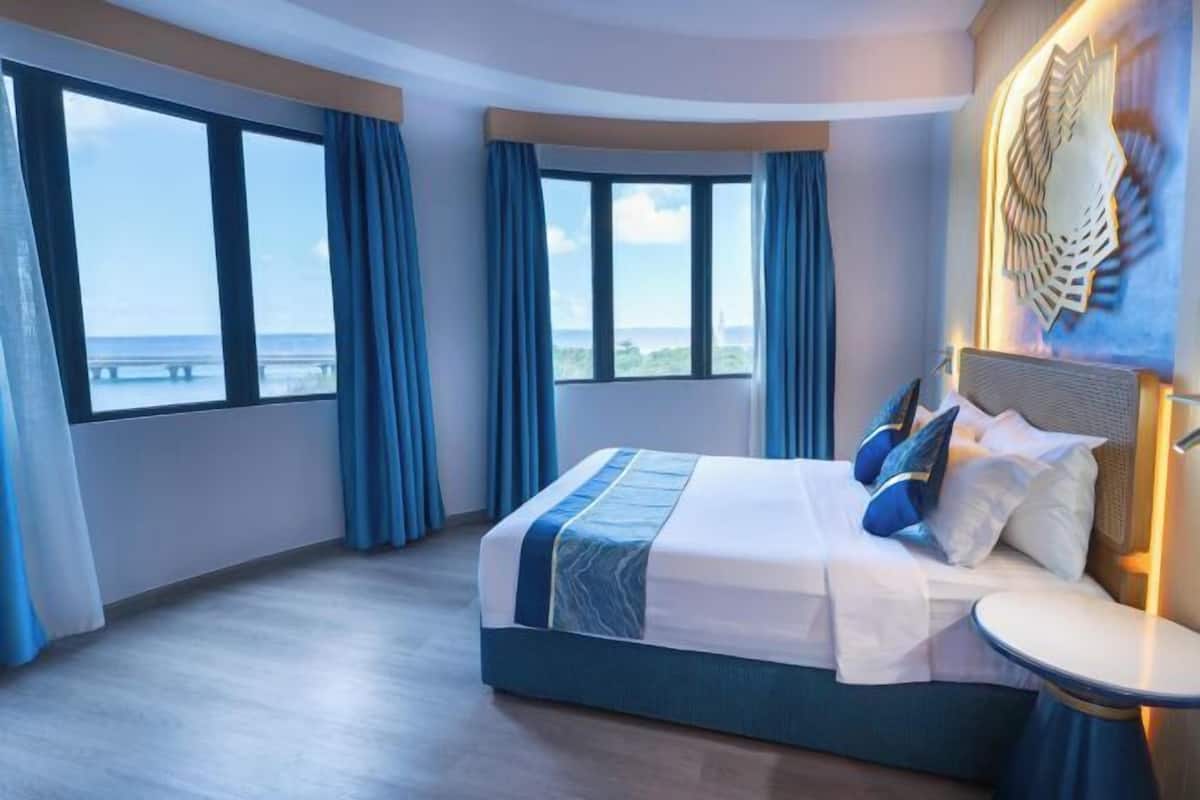 A hotel room with a large bed, a round table, and a view of the sea.