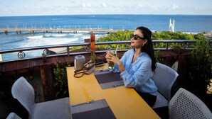 A woman sitting at a table with a view of the ocean and a bridge in the background.