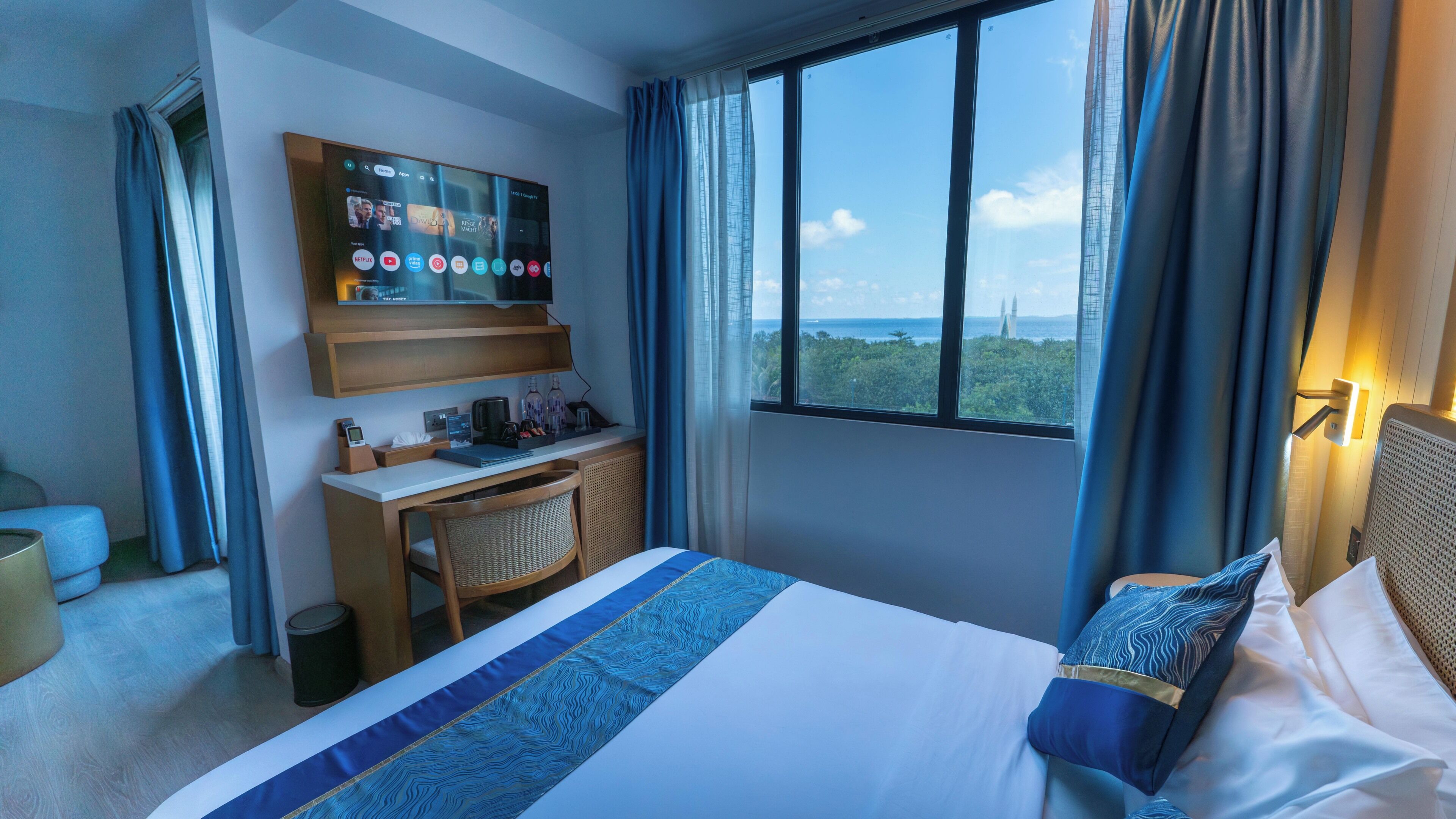 A hotel room with a bed, a desk, a TV, and a window with a view.