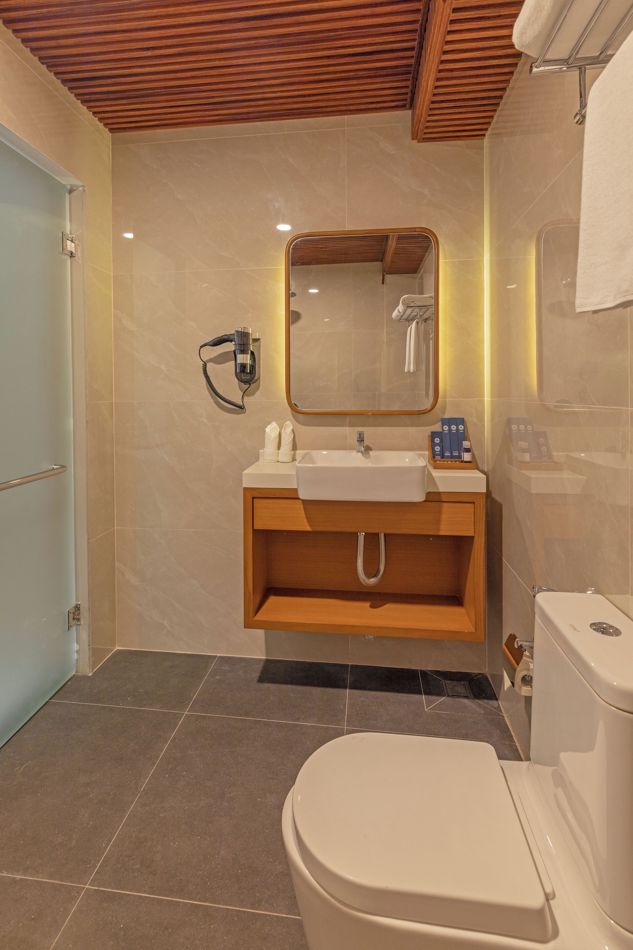 A modern bathroom with a wooden vanity, a sink, a mirror, and a toilet.