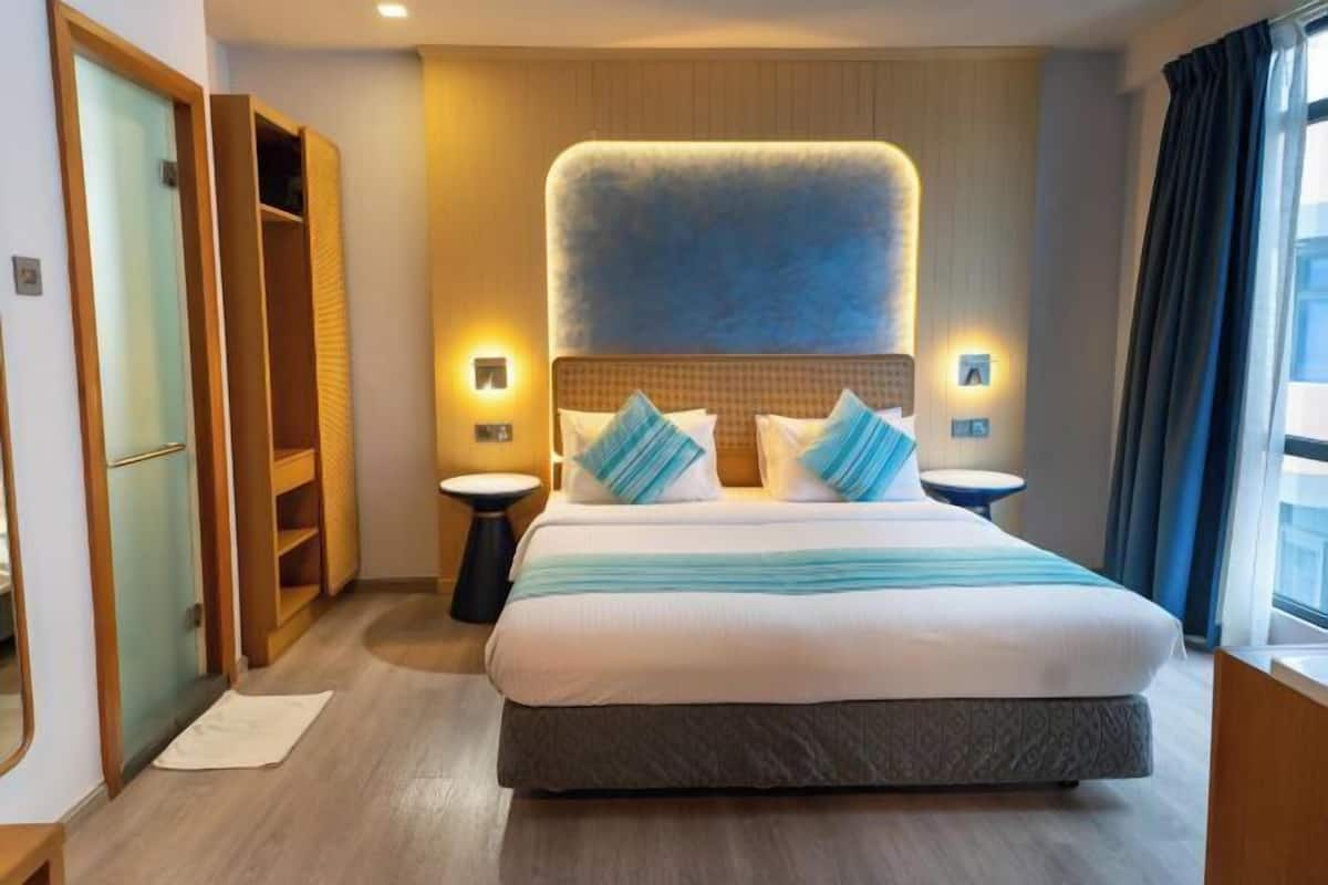 A hotel room with a large bed, bedside tables, a wardrobe, and a view of the city.