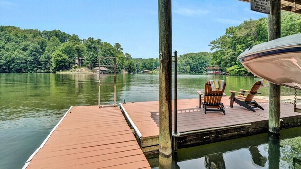 Une jetée en bois, dotée de chaises et d’un espace abrité, offre une vue sur un lac paisible, avec une végétation luxuriante en arrière-plan.