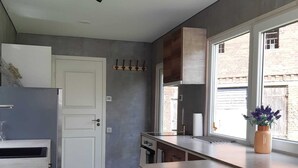 Une cuisine moderne dotée d’un réfrigérateur encastré, d’un plan de travail en bois, de tabourets de bar et d’une fenêtre donnant sur un immeuble en briques.