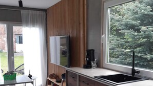 Une cuisine moderne dotée d’une grande fenêtre, de meubles en bois, d’un four encastré et d’une machine à café posée sur le plan de travail.