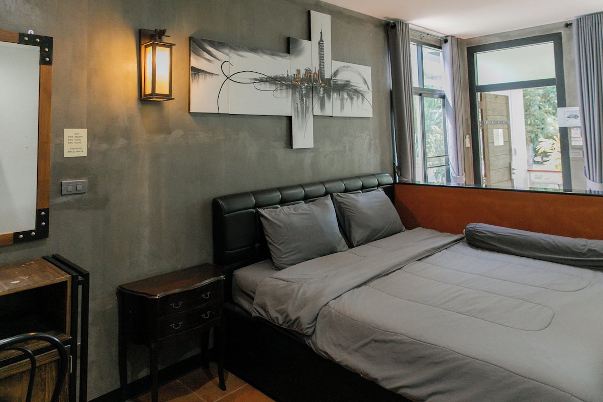 A bedroom with a bed, a nightstand, a desk, and a wall-mounted lamp.