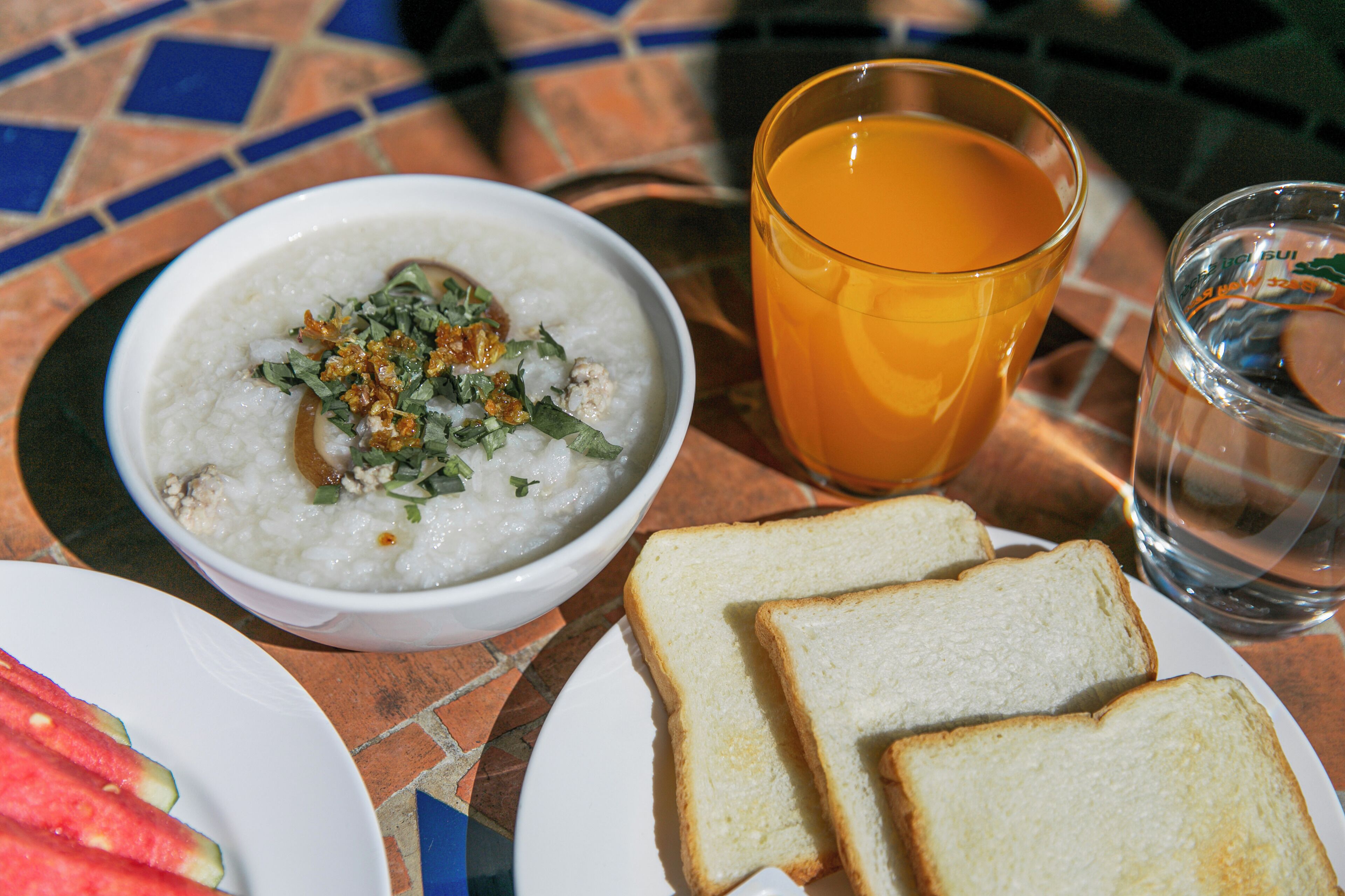 Une table avec un bol de riz, des tranches de pain, un verre de jus d’orange et un verre d’eau.