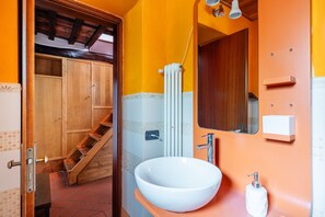 Un baño con lavabo blanco, escalera de madera y zona de ducha con azulejos.