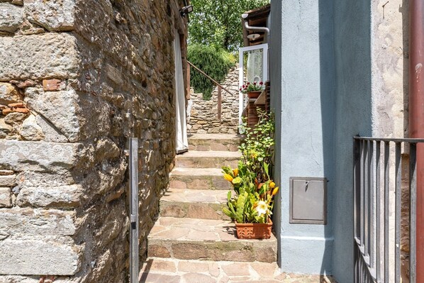 A stone staircase leading to a door with a window, surrounded by potted plants and a metal railing. - Holiday Home 'Casa Del Rio' with Garden & Wi-Fi (Capannori)