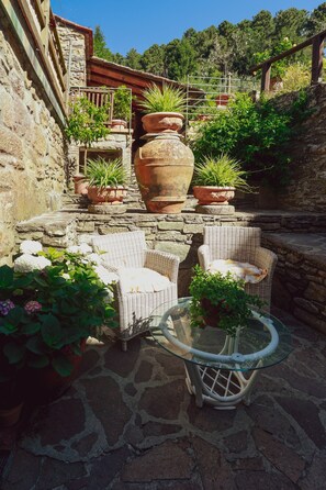 Une terrasse en pierre avec des meubles en osier et des plantes en pot.