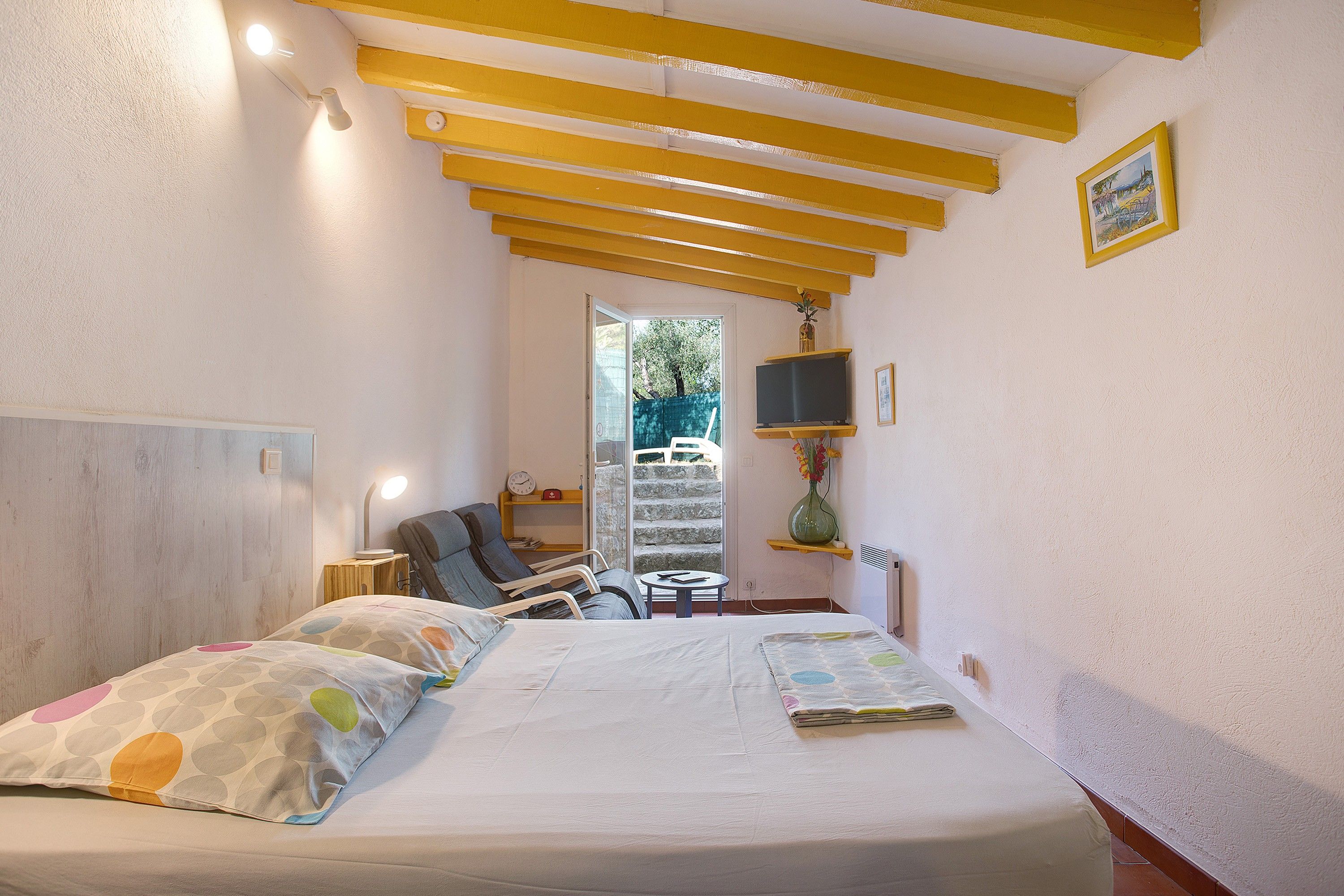 Un dormitorio con cama, mesita de noche, lámpara, silla y vistas al exterior.