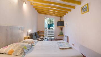 Un dormitorio con cama, mesita de noche, lámpara, silla y vistas al exterior.