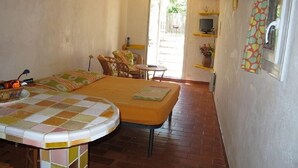 A room with a bed, a small table, a chair, a television, and a window with a curtain.