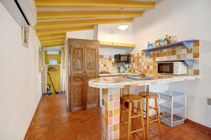 A compact kitchen with a tiled backsplash, a microwave, a coffee maker, and a small bar stool.