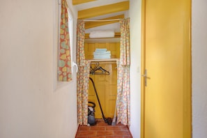 A narrow hallway with a yellow door, a laundry area with hanging clothes, and a vacuum cleaner. - Studio Apartment 'Meublé' with Shared Pool, Private Garden and Wi-Fi (Lorgues)