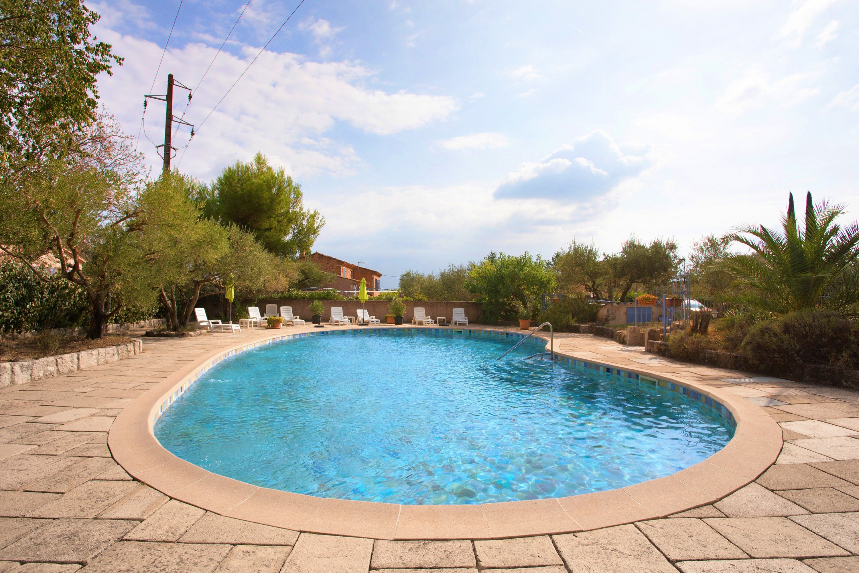A swimming pool with a tiled edge, surrounded by lounge chairs and potted plants.
