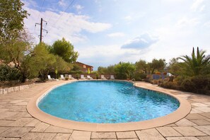A swimming pool with a tiled edge, surrounded by lounge chairs and potted plants.