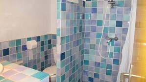 A bathroom with a shower, toilet, and a sink with a tiled countertop.