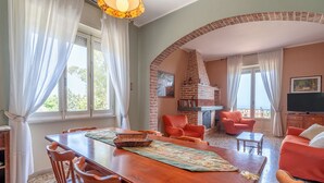 Il y a un coin repas avec une table en bois, des chaises et un plateau de service. Le salon est doté d’une cheminée en briques, de canapés orange et d’un téléviseur.