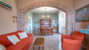 Un salon doté d’une arche en briques, d’un canapé rouge, d’une table basse en bois et d’un coin repas avec une cheminée en briques.